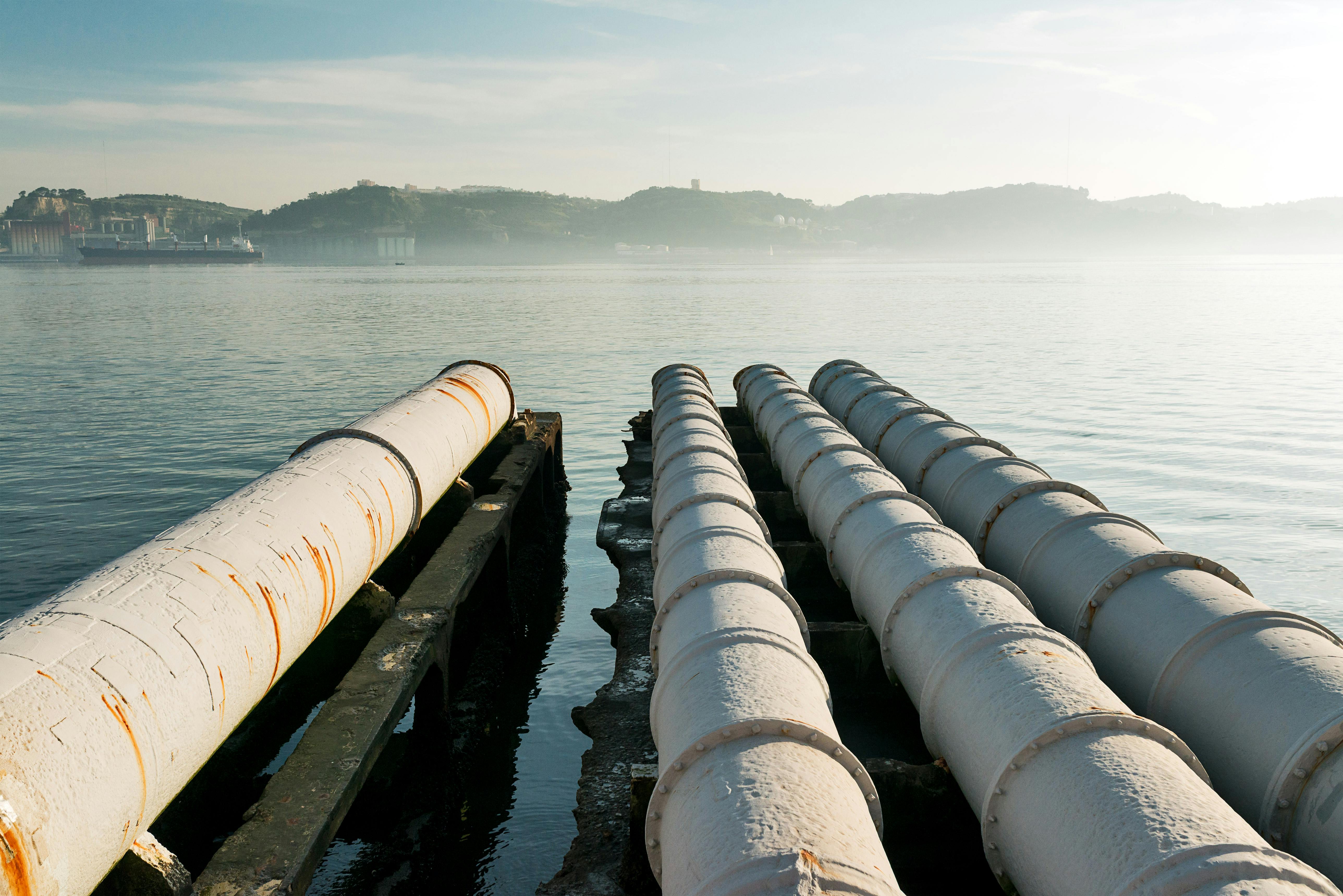 Industrial pipelines extending into the sea at sunset.